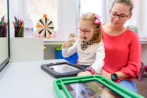 Pädagogische Fachkraft begleitet ein Kind bei der Nutzung eines Tablets.